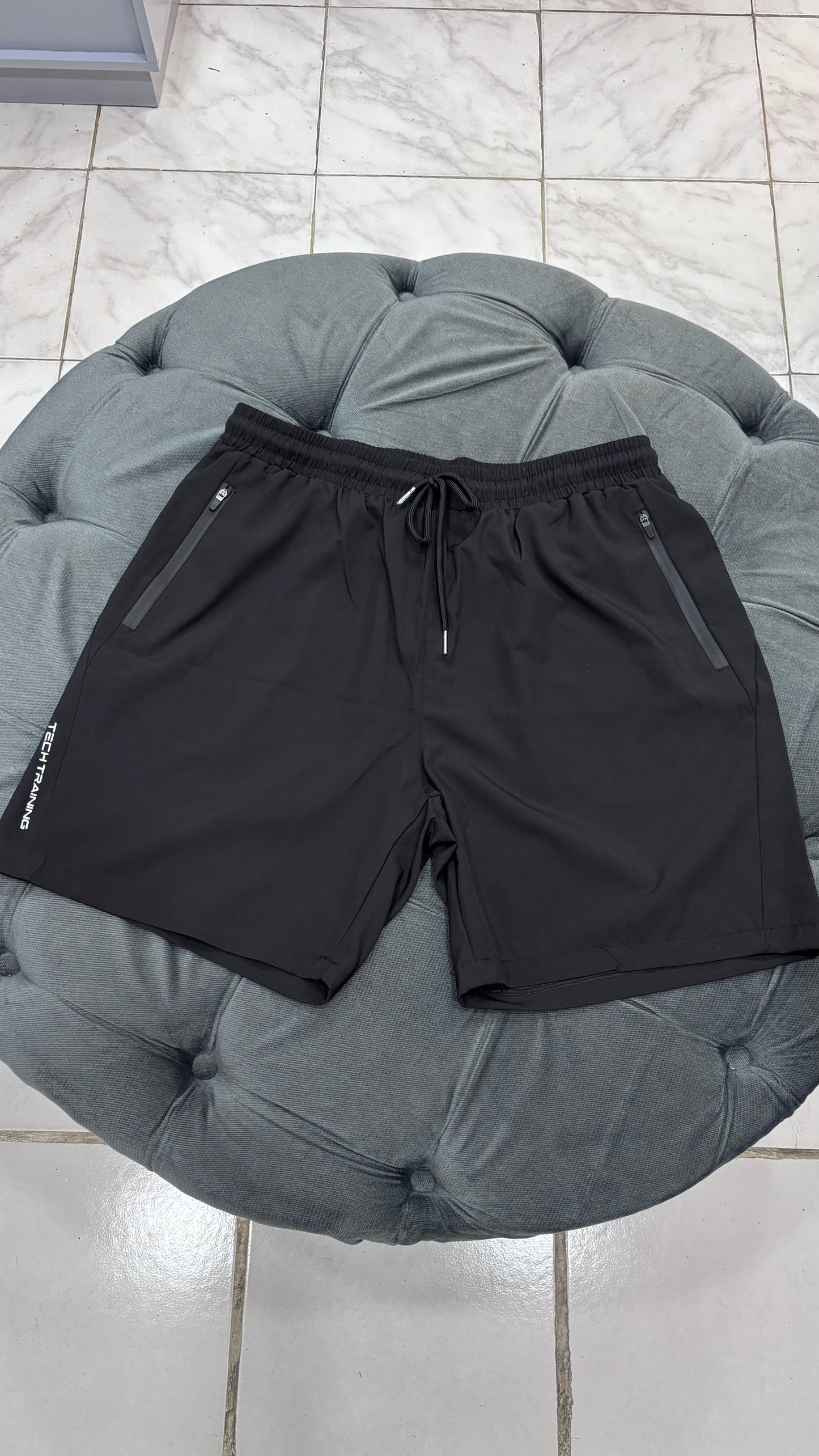 Short impermeable con cierre en los bolsillos y letras blancas a los costados de caballero deportivo Negro